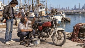 Un hombre mayor arrodillado junto a una moto limpia una bujía mientras un joven con el casco en la mano lo mira, en el muelle de pescadores.