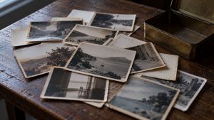 Fotografías antiguas en blanco y negro esparcidas sobre una mesa de madera, junto a una caja de latón abierta
